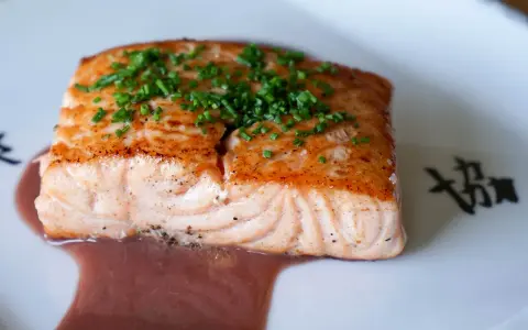 Un filet de saumon cuit, garni de ciboulette, baignant dans une sauce rouge. Un délice qui invite à se demander quel vin rouge avec du saumon cuit serait parfait.