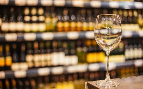Verre à vin vide sur un comptoir, devant des étagères remplies de bouteilles. L'ambiance évoque une foire aux vins de printemps.
