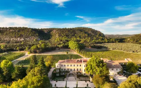 Vue aérienne du **château Beaulieu**, un domaine viticole pittoresque entouré de vignobles et d'une colline boisée. On imagine Nicolas **Sarkozy** y savourer un bon vin.