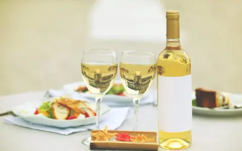 Une bouteille de vin blanc et deux verres sur une table, avec des salades et un dessert. Un clin d'œil à Alexandre de Lur Saluces.