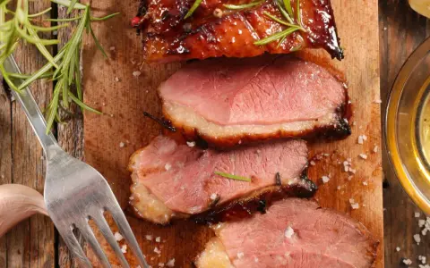 Tranches de magret de canard juteux, garnies de romarin et de sel, prêtes à être dégustées avec un verre de vin.