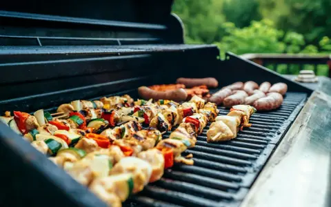 Brochettes de poulet et légumes grillés sur un barbecue, accompagnées de saucisses. Parfait pour un barbecue d'été avec un verre de vin blanc.