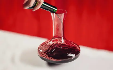 Une main verse un vin rouge profond dans une carafe. Ce pourrait être le meilleur vin du Cabardès, prêt à être savouré.
