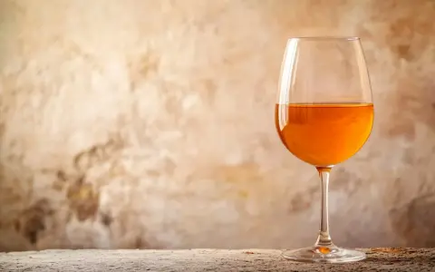 Verre de vin de macération à la couleur ambrée, sur un fond texturé et une table en bois.