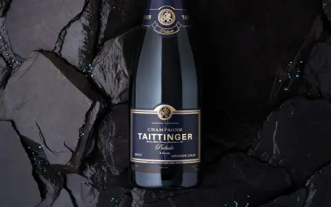 Bouteille de champagne Taittinger Prélude Grands Crus sur fond sombre, avec des paillettes scintillantes. Un avis sur ce champagne est à découvrir.