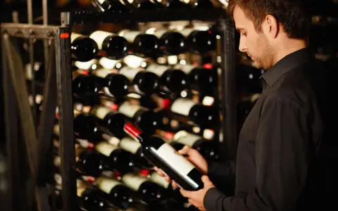 Un homme examine une bouteille de vin dans une cave. Une belle opportunité d'investir dans le vin.