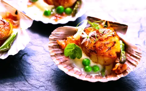 Saint-jacques poêlées, tendres et dorées, servies dans leur coquille avec des petits pois et une touche de vin rouge.