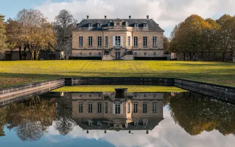 Le château La Louvière, majestueux, se reflète dans un étang paisible, entouré d'arbres aux couleurs d'automne.
