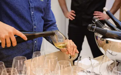 Un homme verse du vin blanc, peut-être un pinot gris, dans un verre. Il sera parfait avec du poisson.