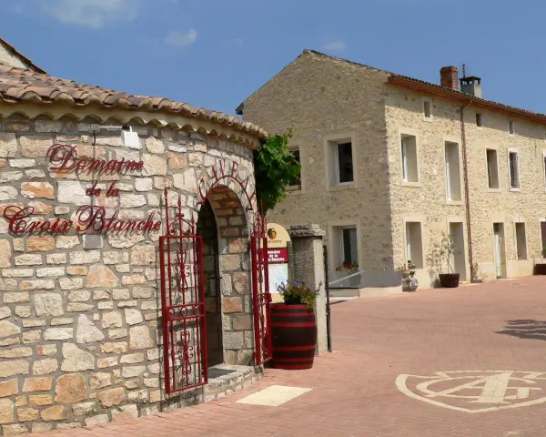 Bienvenue au **domaine de la Croix Blanche**. Une bâtisse en pierre avec une enseigne élégante et une porte ornée de ferronneries rouges.