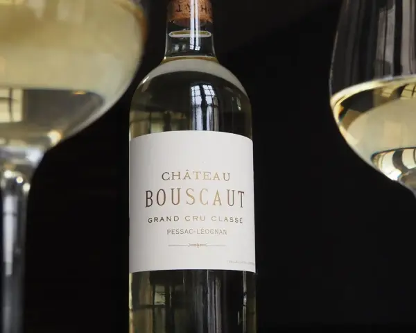 Bouteille de vin blanc Château Bouscaut Pessac-Léognan entre deux verres de vin.
