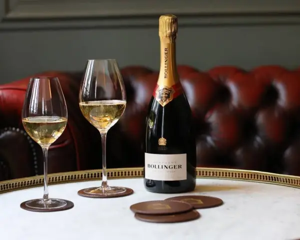 Bouteille de champagne Bollinger et deux verres remplis de champagne sur un plateau, avec un canapé en cuir rouge en arrière-plan.