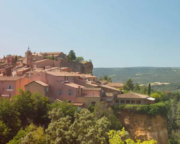 Village perché aux toits de tuiles roses, entouré de verdure. Au loin, des collines rappellent les vignes oubliées d'une Provence intemporelle.