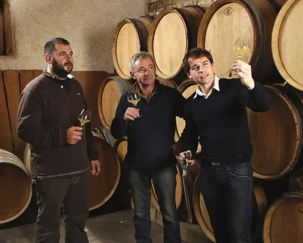 Trois hommes dégustent du vin dans la cave du domaine des Gandines, entourés de fûts de chêne.