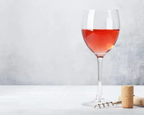Un verre de bon rosé, prêt à être dégusté, avec un tire-bouchon et un bouchon à proximité.