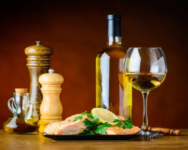 Un plat de saumon avec citron et persil, accompagné d'une bouteille et d'un verre de vin blanc, moulin à poivre et salière, huile d'olive. Le meilleur vin blanc pour cuisiner est prêt.