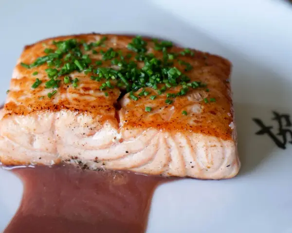 Un filet de saumon cuit, garni de ciboulette, baignant dans une sauce rouge. Un délice qui invite à se demander quel vin rouge avec du saumon cuit serait parfait.