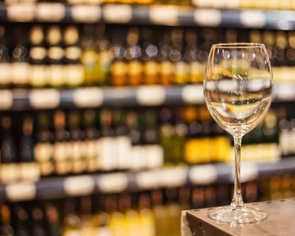 Verre à vin vide sur un comptoir, devant des étagères remplies de bouteilles. L'ambiance évoque une foire aux vins de printemps.