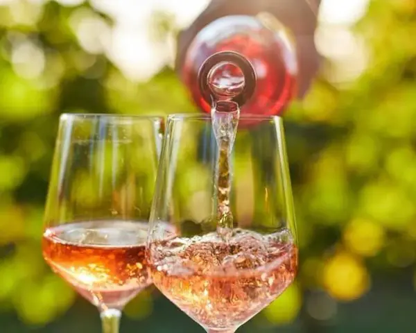 Un verre de rosé est servi dans un autre verre, sous un soleil radieux. Un moment parfait pour boire du rosé tous les jours.