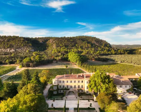 Vue aérienne du **château Beaulieu**, un domaine viticole pittoresque entouré de vignobles et d'une colline boisée. On imagine Nicolas **Sarkozy** y savourer un bon vin.
