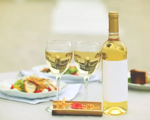 Une bouteille de vin blanc et deux verres sur une table, avec des salades et un dessert. Un clin d'œil à Alexandre de Lur Saluces.