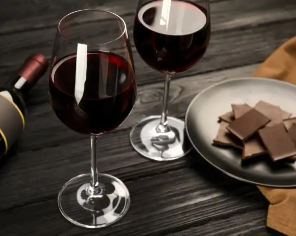 Deux verres de vin rouge, une bouteille et une assiette de chocolat, prêts pour un accord vin chocolat parfait.