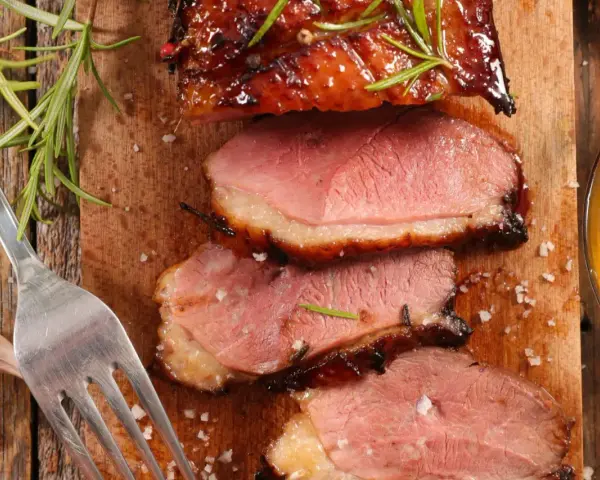 Tranches de magret de canard juteux, garnies de romarin et de sel, prêtes à être dégustées avec un verre de vin.
