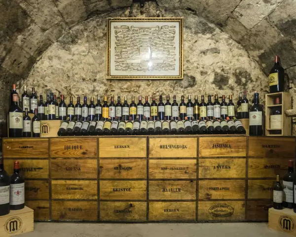 Cave à vin de la côte de Beaune, remplie de bouteilles et de caisses en bois étiquetées avec des noms de villes.