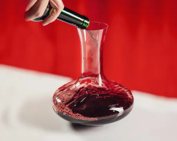Une main verse un vin rouge profond dans une carafe. Ce pourrait être le meilleur vin du Cabardès, prêt à être savouré.