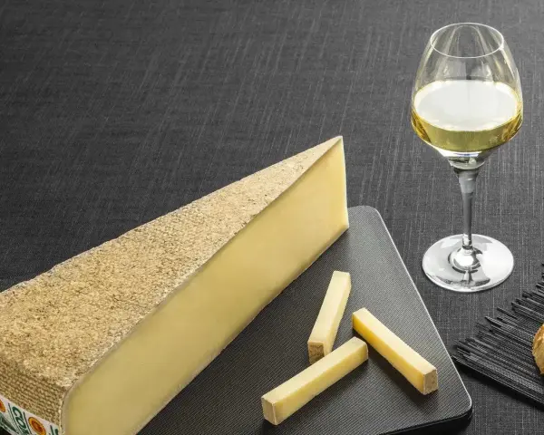 Un morceau de fromage à pâte dure et quelques bâtonnets, accompagnés d'un verre de vin blanc sucré et d'une tranche de pain.