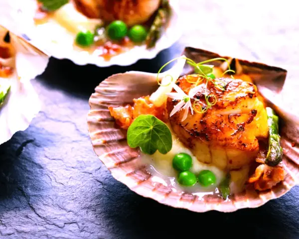 Saint-jacques poêlées, tendres et dorées, servies dans leur coquille avec des petits pois et une touche de vin rouge.