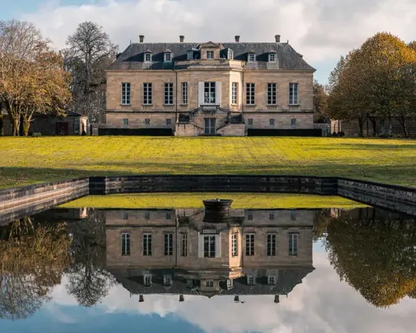 Le château La Louvière, majestueux, se reflète dans un étang paisible, entouré d'arbres aux couleurs d'automne.