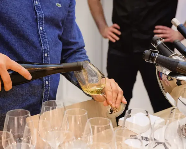 Un homme verse du vin blanc, peut-être un pinot gris, dans un verre. Il sera parfait avec du poisson.