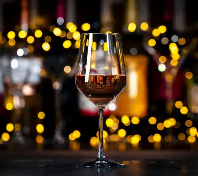 Un verre de vin orange scintille, reflétant les lumières chaudes d'un bar animé.