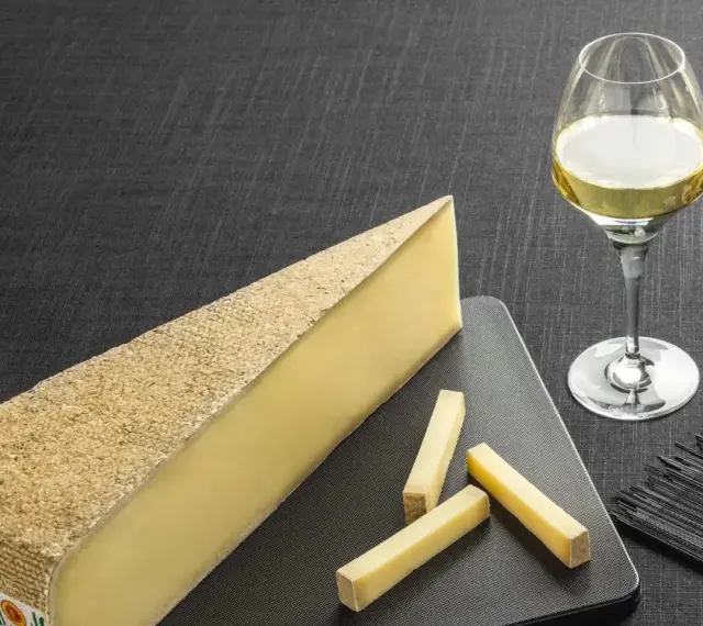 Un morceau de fromage à pâte dure et quelques bâtonnets, accompagnés d'un verre de vin blanc sucré et d'une tranche de pain.