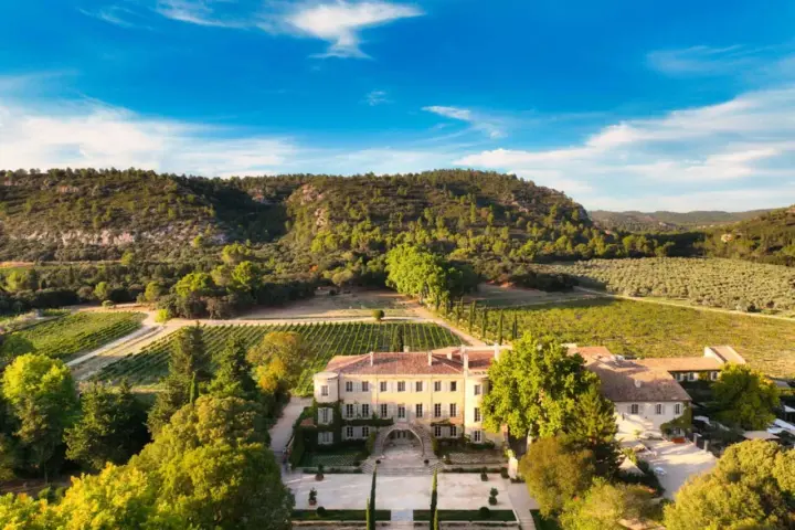 Vue aérienne du **château Beaulieu**, un domaine viticole pittoresque entouré de vignobles et d'une colline boisée. On imagine Nicolas **Sarkozy** y savourer un bon vin.