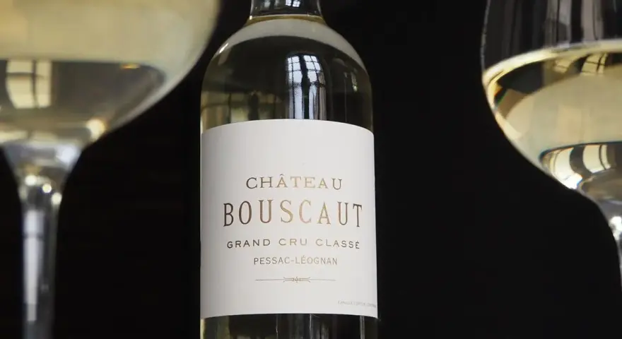 Bouteille de vin blanc Château Bouscaut Pessac-Léognan entre deux verres de vin.