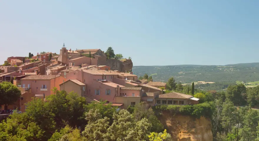 Village perché aux toits de tuiles roses, entouré de verdure. Au loin, des collines rappellent les vignes oubliées d'une Provence intemporelle.