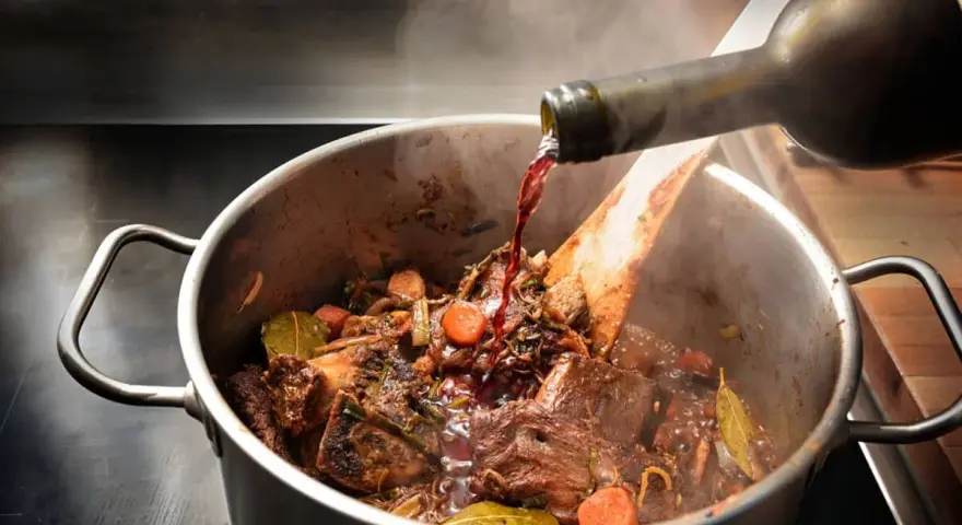 Un vin rouge est versé dans un plat mijoté de bœuf, carottes et herbes. Quel vin bourguignon sublimera ce plat ?