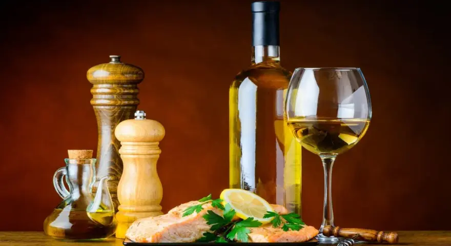 Un plat de saumon avec citron et persil, accompagné d'une bouteille et d'un verre de vin blanc, moulin à poivre et salière, huile d'olive. Le meilleur vin blanc pour cuisiner est prêt.