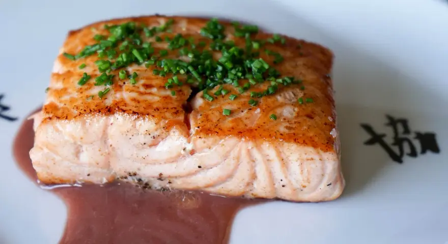 Un filet de saumon cuit, garni de ciboulette, baignant dans une sauce rouge. Un délice qui invite à se demander quel vin rouge avec du saumon cuit serait parfait.