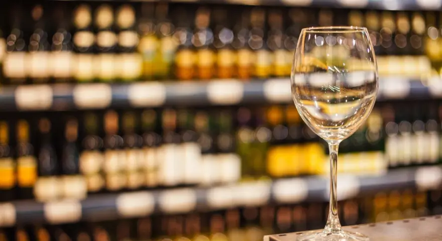 Verre à vin vide sur un comptoir, devant des étagères remplies de bouteilles. L'ambiance évoque une foire aux vins de printemps.