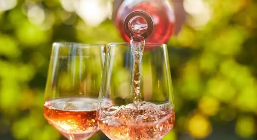 Un verre de rosé est servi dans un autre verre, sous un soleil radieux. Un moment parfait pour boire du rosé tous les jours.