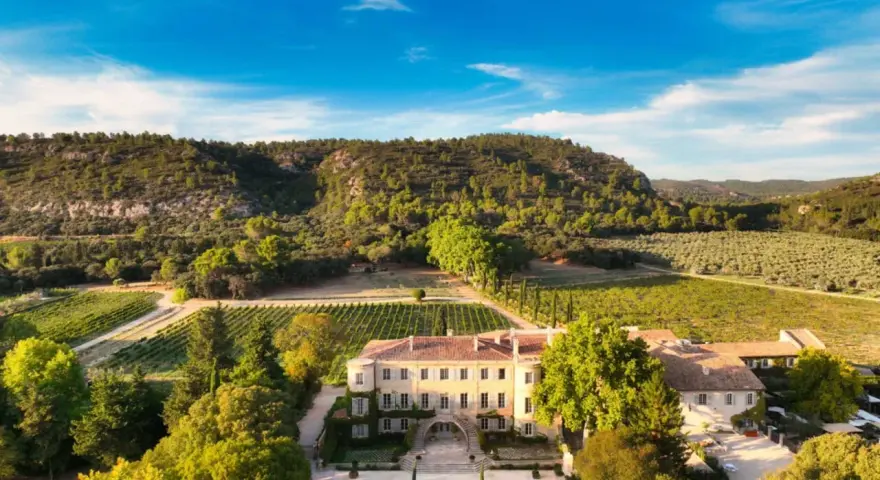 Vue aérienne du **château Beaulieu**, un domaine viticole pittoresque entouré de vignobles et d'une colline boisée. On imagine Nicolas **Sarkozy** y savourer un bon vin.