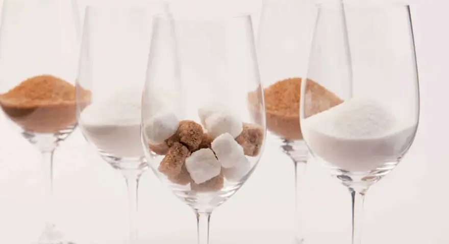 Cinq verres à vin contiennent différentes formes de sucre : du sucre en poudre blanc, du sucre brun en poudre et des morceaux de sucre blanc et brun. Une métaphore visuelle du sucre dans le vin.
