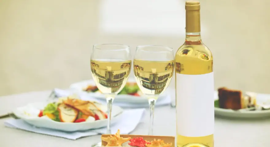 Une bouteille de vin blanc et deux verres sur une table, avec des salades et un dessert. Un clin d'œil à Alexandre de Lur Saluces.