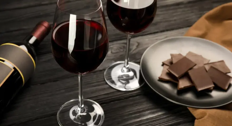 Deux verres de vin rouge, une bouteille et une assiette de chocolat, prêts pour un accord vin chocolat parfait.