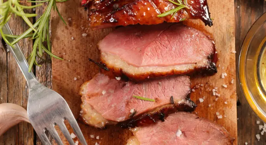 Tranches de magret de canard juteux, garnies de romarin et de sel, prêtes à être dégustées avec un verre de vin.