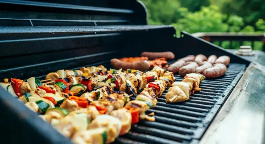 Brochettes de poulet et légumes grillés sur un barbecue, accompagnées de saucisses. Parfait pour un barbecue d'été avec un verre de vin blanc.