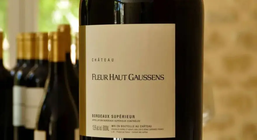 Bouteille de vin rouge Château Fleur Haut Gaussens, Bordeaux Supérieur, avec d'autres bouteilles en arrière-plan.